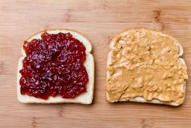 Simple peanut butter and jelly sandwich with strawberry jam and chunky peanut butter on white bread, separated and placed on a bamboo cutting board with soft natural window light.